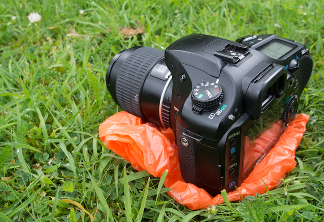 Pentax K-5 on shopping bag to protect from wet grass